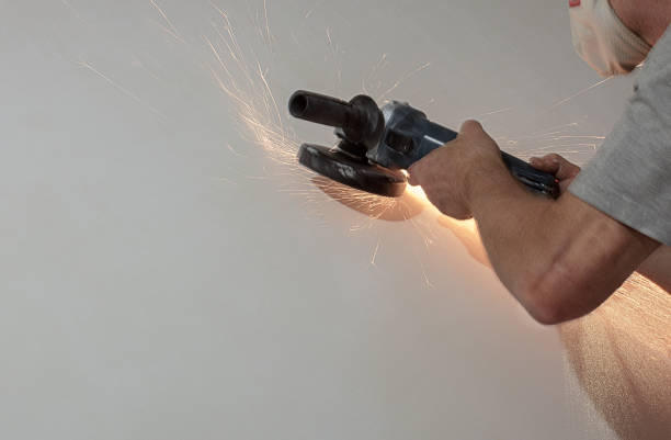 A man uses a grinder to remove unnecessary items on the wall. Bright sparks illuminate the wall. The apartment is being renovated. amoladora de troqueles— una amoladora de troqueles neumática con un cabezal de ángulo recto. una amoladora de troqueles es una herramienta eléctrica de mano utilizada para moler, lijar, pulir, pulir o material de máquina, generalmente metal, pero tam