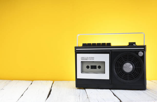 ein alter kassettenrekorder aus den 1970er jahren steht auf einem holztisch vor gelbem hintergrund. - recording tape stock-fotos und bilder