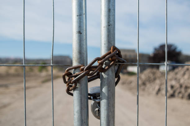 Metal chain is padlocked and provides security at a fence. The entrance to a construction site is closed. rusty fence stock pictures, royalty-free photos & images