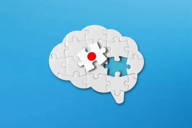 Photo of Japanese learning concept, white jigsaw puzzle pieces with japanese flag a human brain shape on blue background