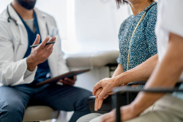 Senior couple meeting with a medical doctor at a hospital A photo showing a senior couple holding hands while seated across a doctor. The doctor's hand can be seen gesturing as he is talking to the couple. obscured face stock pictures, royalty-free photos & images