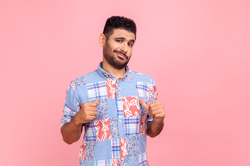 This is me! Portrait of egoistic arrogant selfish man with beard in blue shirt pointing himself, boasting successful achievement, feeling proud. Indoor studio shot isolated on pink background.