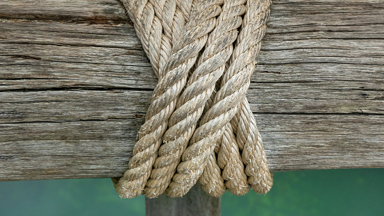 Ropes wrapped around an old, weathered beam. In the background green water of a lake