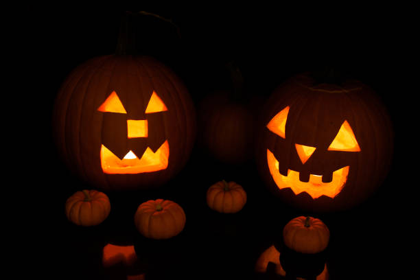 istock Two big handcrafted Halloween Jack O' lanterns illuminated by candle on a black background in darkness 1337073199