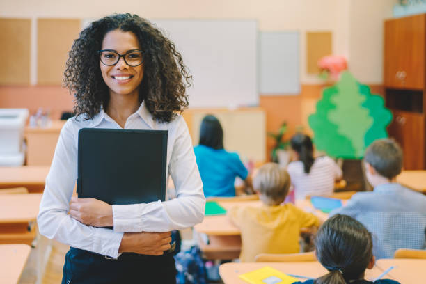 The classroom is filled with happiness as the smiling educator conducts a lesson near the blackboard. he standing professor in the classroom uses the board to explain a complex topic.