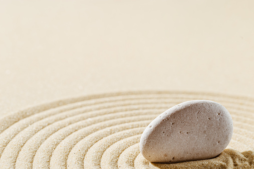 Aesthetic minimal background with zen stones on sand. Pattern in Japanese Zen Garden with concentric circles around white around stone cairn for meditation and tranquility.