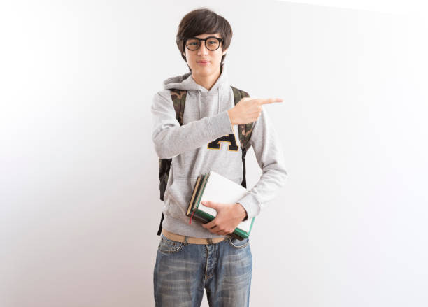 istock Handsome teen boy students carrying a backpack pointing finger standing on white background. 1337081793