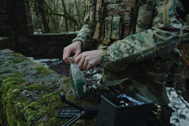 portrait of airsoft player in professional equipment loads a gun with bullets in the forest. soldier with weapons at war - airsoft gun imagens e fotografias de stock