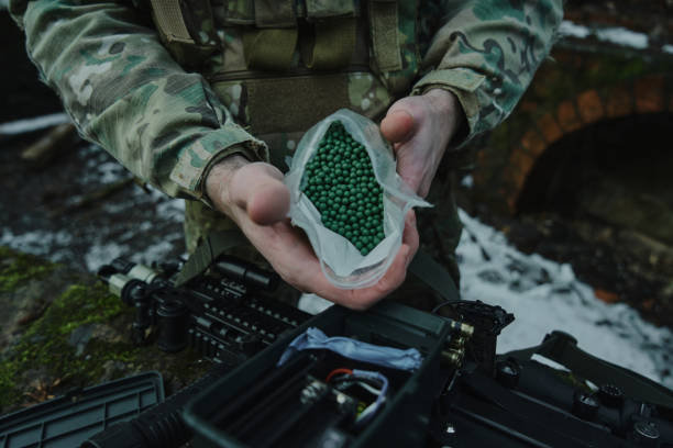 porträt eines airsoft-spielers in professioneller ausrüstung lädt eine waffe mit kugeln in den wald. soldat mit waffen im krieg - airsoft stock-fotos und bilder