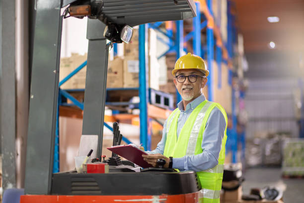 Asian Chinese senior warehouse worker operating forklift working in industry factory stock photo