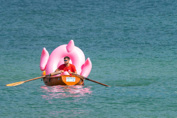 socorrista de playa remando en su bote llevando un gran flamenco inflable rosa. - lifeguard orange nature beach fotografías e imágenes de stock