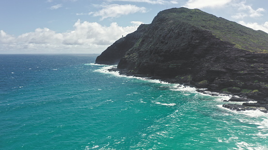 Flying over Makapuu Beach Park. Giant waves foaming and splashing in the ocean. The turquoise color of the Pacific Ocean water on tropical island. Magnificent mountains of Hawaiian island of Oahu
