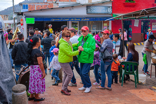 San Francisco, Cundinamarca, Colombia - August 20, 2017: It is Fiesta time in the Cundinamarca town of San Francisco in the Latin American country of Colombia. An older couple are sen dancing on the side walk as a band plays in the background. The elevation at street level is 4990 feet above mean sea level. Photo shot in the early afternoon sunlight; horizontal format.
