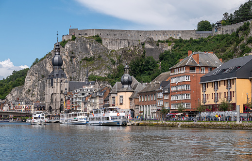 Dinant, Wallonia, Belgium - August 8, 2021: Citadel Fort above downtown upriver right bank with plenty of houses, town hall, and Collégiale Notre Dame church.. Docked river boat.