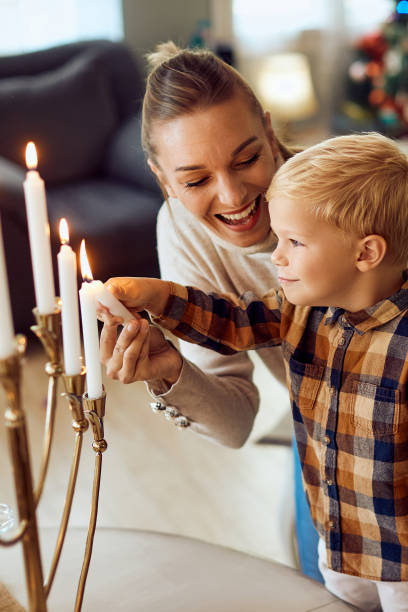 Happy Jewish mother and son lighting up traditional Hanukkah candles at home. Happy little boy and his mother lighting up candles in menorah on Hanukkah at home. judaism photos stock pictures, royalty-free photos & images