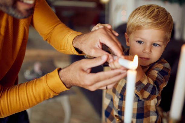 der kleine junge und sein vater blitzen die menora, während sie chanukka zu hause feiern. - six candles stock-fotos und bilder