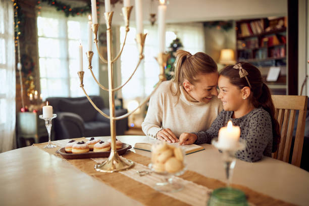 Happy Jewish mother and daughter reading Tanakh during Hanukkah at home. Happy little girl and her mother reading Hebrew bible while celebrating Jewish festival of lights, Hanukkah at home. hanukkah stock pictures, royalty-free photos & images