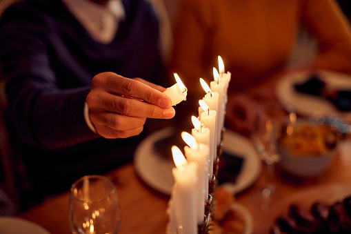 Close-up of Jewish man  lightning the menorah during family dinner at dining table on Hanukkah.