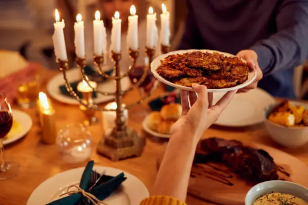 Close-up of couple passing latkes during a meal at dining table while celebrating Hanukkah at home.