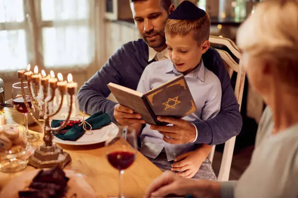 Jewish father and son reading Hebrew bible before family dinner during Hanukkah.