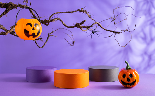 Halloween party concept. Podiums or pedestals for products display and pumpkin buckets for candies over purple background. Halloween holiday decorations.