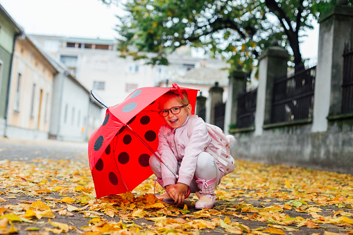 School girl with ladybug umbrella playing on the autumn street.