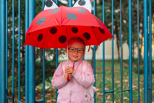 Girl with red umbrella standing in front of the school yard.