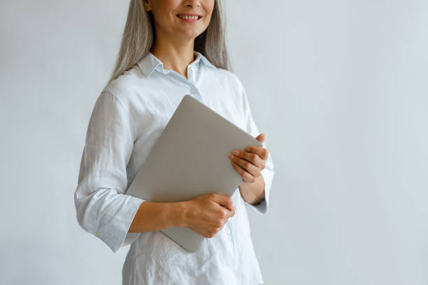 istock Smiling middle aged lady holds laptop on light grey background 1337111771