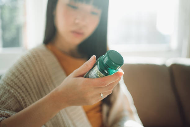 mulher asiática escolhendo entre suplementos - vitamin pill nutritional supplement pill bottle - fotografias e filmes do acervo