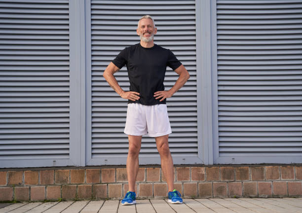 istock Full length shot of active middle aged man in good shape smiling while standing with arms on waist, posing outdoors over gray background 1337118539