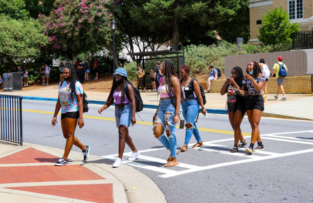 A group of female students in a crosswalk at a university campus with other students waiting at a bus stop in the background. stock photo