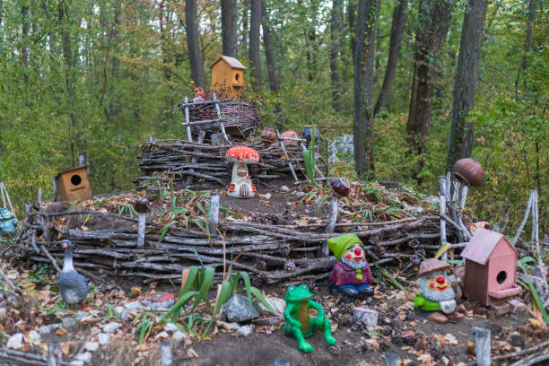 A decorative trash bin resembling a whimsical face stands next to a wooden fence, surrounded by fallen leaves, adding character to the garden area in autumn.
