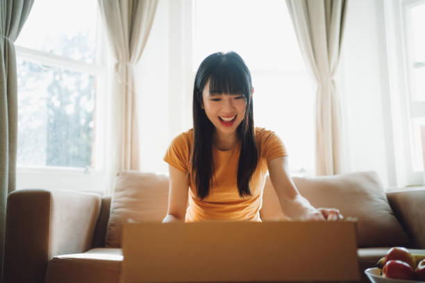 giovane donna sorridente che apre una scatola di consegna nel soggiorno - unboxing foto e immagini stock