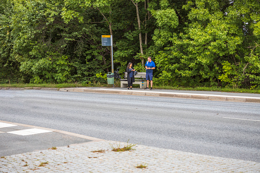 Sweden. Uppsala. 08.29.2021. Beautiful view of woman and man surfing on mobiles awaiting buss on public buss stop.