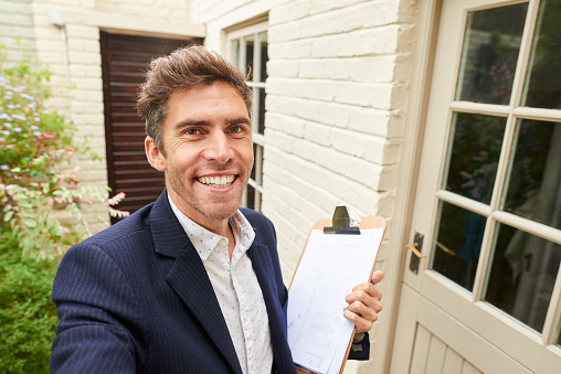 Smiling male real estate agent talking a seflie video for a walk-through of a home for sale