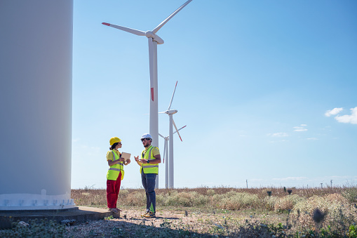 Two workers standin and discussing work plan on a wind turbines farm