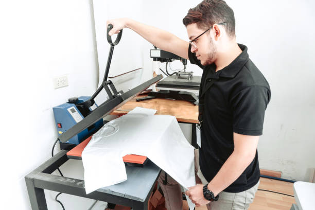 istock young latinx man uses a t-shirt sublimation machine. Hispanic worker using an iron sublimation for a white t-shirt. designs concept. 1337149356