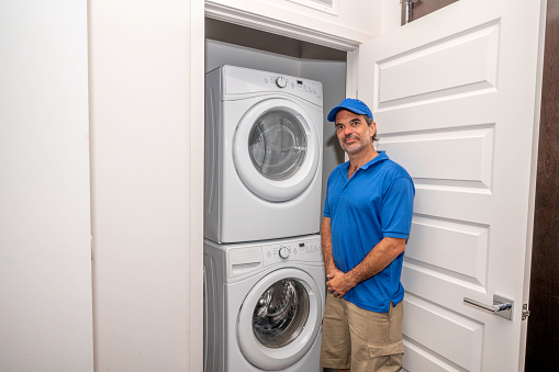 Appliance technician standing next to a modern washing machine and dryer in a small laundry room