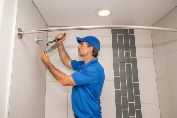 A plumber working on a showerhead in a modern bathroom