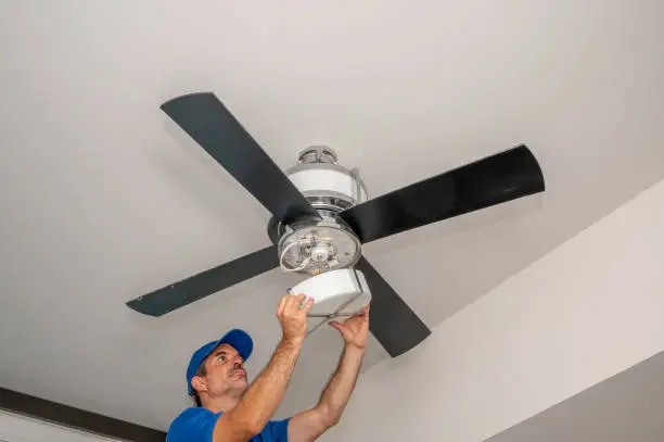 Man removes glass light cover on a ceiling fan inside of a home