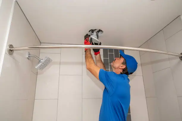 An electrician works on a light fixture on the ceiling of a bathroom