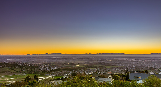 This July 2021 sunset photo shows the city of Ōtautahi Christchurch, Aotearoa New Zealand. The vantage point is the Cashmere Hill Lookout, Cracroft Reserve in the Port Hills. The urban sprawl of the foreground fades into the snow-capped Te Tiritiri-o-te-moana Southern Alps which run the length of Te Waipounamu South Island.