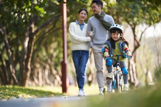 happy little asian girl riding bike in park - helmet bicycle little girls child imagens e fotografias de stock