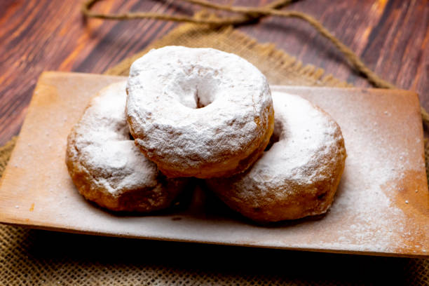 istock Delicious donuts with powdered sugar on wooden plate 1337160849
