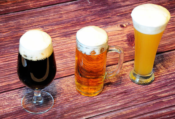 three different glasses with different types of beer, light, dark and wheat on a wooden table. - rustic beer brewery indoors imagens e fotografias de stock