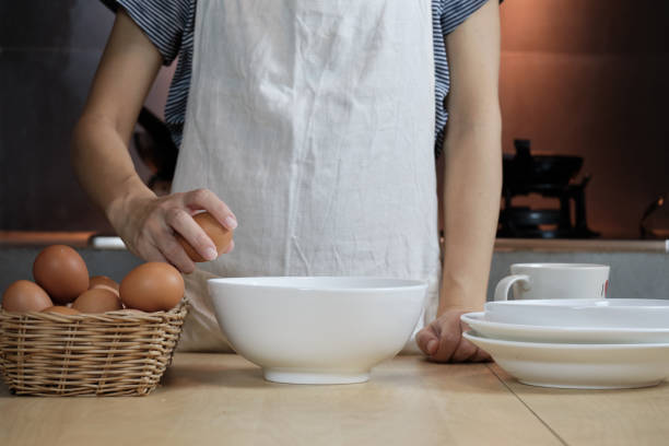 istock Female cook in a white apron is cracking an egg in home's kitchen. 1337164433