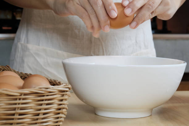 흰 앞치마를 입은 여성 요리사가 집 부엌에서 달걀을 부수고 있습니다. - eggs bowl cracked dining table 뉴스 사진 이미지