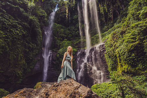 Woman in turquoise dress at the Sekumpul waterfalls in jungles on Bali island, Indonesia. Bali Travel Concept.