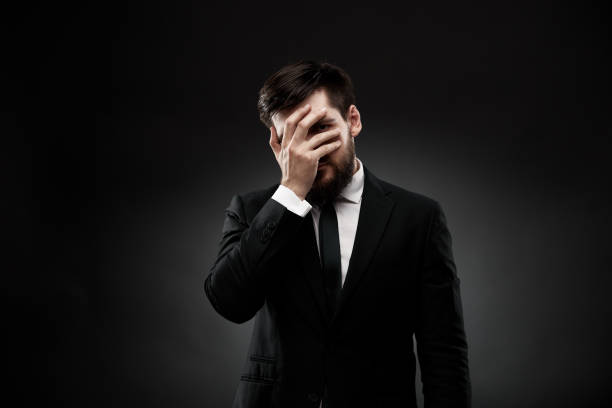 Tired businessman covering face with hand, hiding stock photo