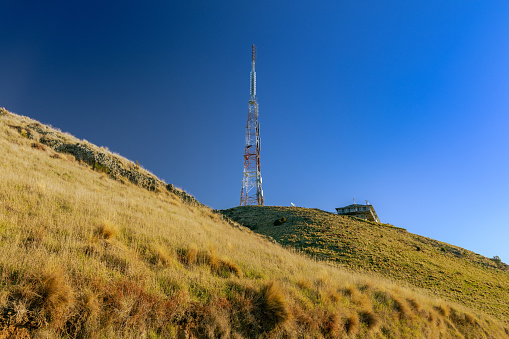 This July 2021 photo shows the Sugarloaf Communications Tower high above Ōtautahi Christchurch, Aotearoa New Zealand. The television and radio transmission site built in the 1960s is located in the Port Hills on Horomaka Banks Peninsula. It overlooks the Canterbury Plains and the city centre on one side, and Te Whakaraupō Lyttelton Harbour on the other side. The tower is operated by Kordia, a New Zealand government-owned entity.